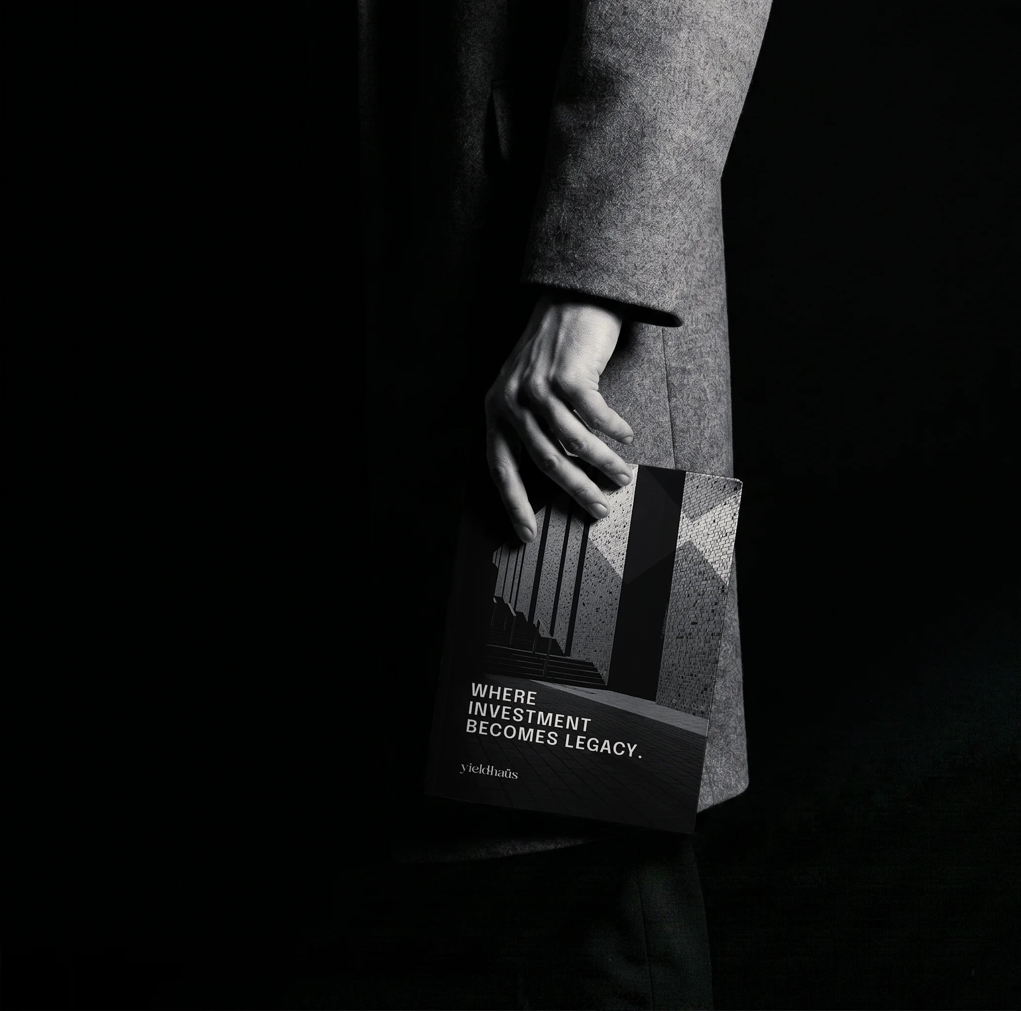 Hand holding the Yieldhaüs book printed “WHERE INVESTMENT BECOMES LEGACY.”