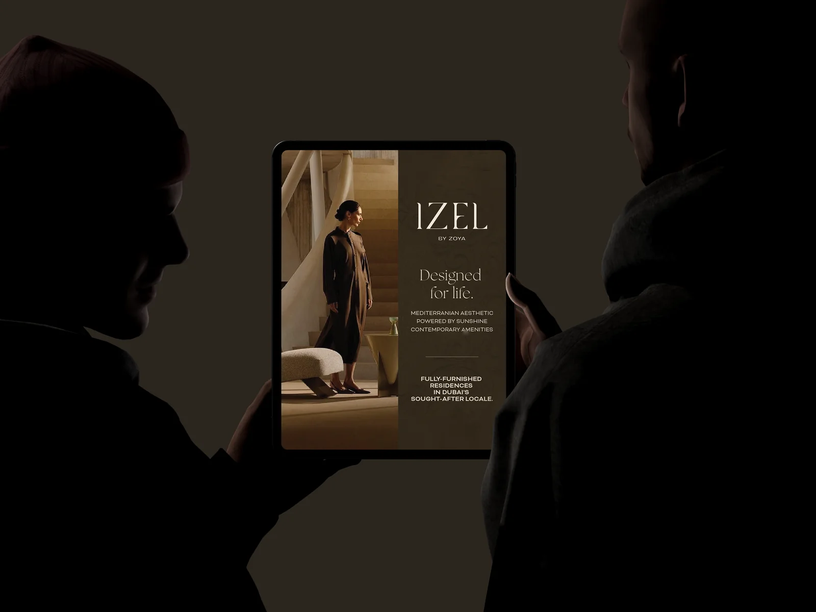 Two silhouettes holding a tablet showing the Izel by Zoya site