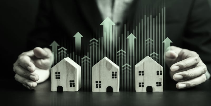 Businessman shielding house models with growth arrows, real estate market growth
